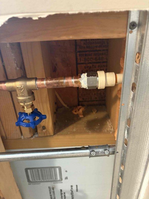 Installed new spigot assembly with copper piping and blue-handled ball valve shut-off within wall cavity. Accessed interior plumbing through existing opening, connected copper pipe to brass fittings, and integrated flexible stainless steel tubing to complete water supply line installation.