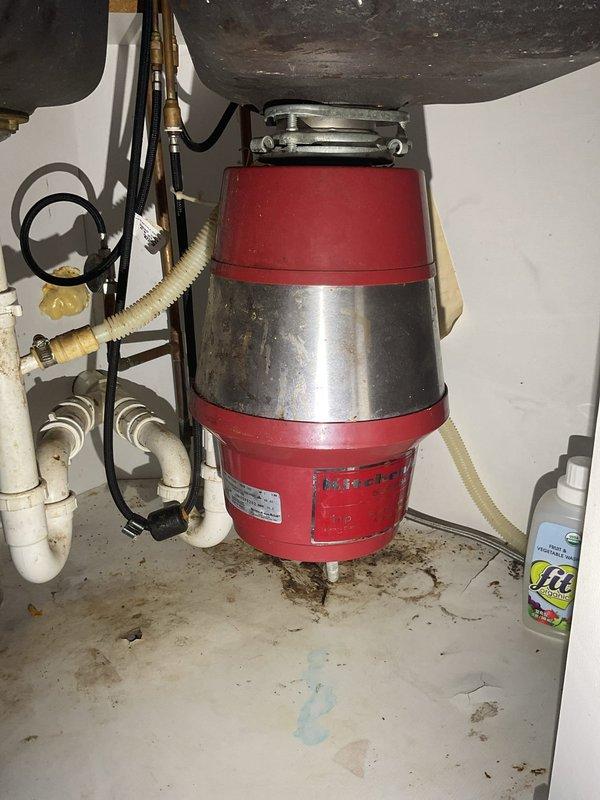 Completed installation of new garbage disposal unit under kitchen sink. Mounted red and stainless steel disposal assembly to sink drain with proper electrical connections and plumbing integration. Connected discharge line with corrugated drain hose to existing PVC trap configuration. Verified proper operation of disposal unit and checked all connections for leaks. Installation completed with disposal fully functional and ready for use.
