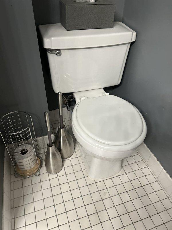 Responded to multiple plumbing concerns in residential bathroom. Addressed foul odor emanating from toilet area, particularly noticeable when exhaust fan operates, indicating potential wax ring failure at toilet base. Diagnosed slow tank refill issue causing 20-minute delay between flushes, likely due to faulty fill valve or supply line restriction. Assessed leaking shower faucet handles requiring replacement. Inspected radiator pipe with seasonal dripping issue during winter months. Documented existing conditions including white two-piece toilet with chrome flush handle, white tile flooring with darkened grout showing age-related wear, and overall bathroom layout for repair planning and parts ordering.