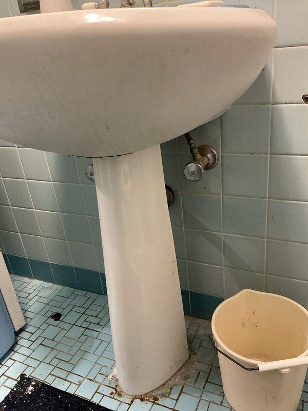 Completed on-site estimate for bathroom renovation in 85-year-old residence requiring installation of two new toilets and one pedestal sink with faucet assembly. Assessed existing plumbing infrastructure and confirmed no new supply or drain piping modifications needed for fixture replacement. Documented current conditions including existing pedestal sink with visible age-related discoloration, deteriorated toilet with heavy interior staining and buildup, vintage tile work with rust staining at floor-to-fixture interfaces, and existing brass shut-off valves requiring evaluation for compatibility with new fixtures.
