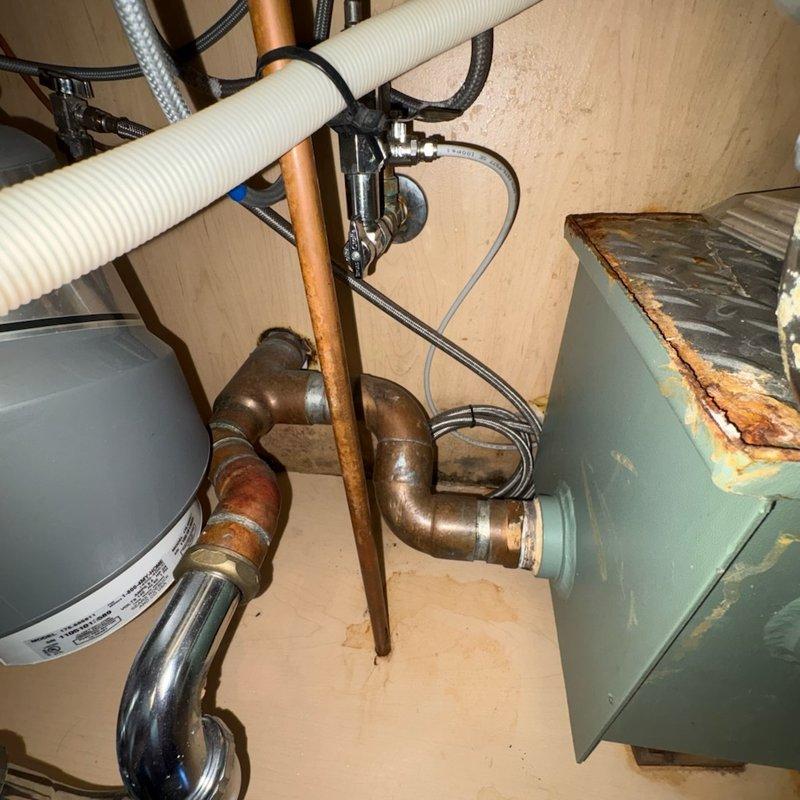 Responded to kitchen sink drainage issue and evaluated existing grease trap assembly beneath sink cabinet. Upon inspection, confirmed presence of outdated grease trap installation connected to disposal unit and drainage system, which was occupying significant cabinet space and had not been maintained in extended period. Assessed plumbing configuration including garbage disposal unit, PVC drainage pipes, and water supply lines to determine feasibility of grease trap removal and system reconfiguration. Documented existing conditions of under-sink plumbing components and mechanical systems for recommended modifications to improve drainage performance and reclaim usable cabinet space.