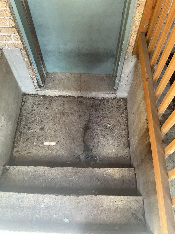 Responded to a slow-draining communal area drain that leads to a catch basin in the back exterior stairwell and patio area of a commercial building. Conducted inspection of the affected ground drain, catch basin, and additional ground drains in the area to assess blockage severity and determine clearing requirements. Documented site conditions with photographs showing the stairwell entrance with floor drain and the brick passageway patio area for estimate preparation purposes.