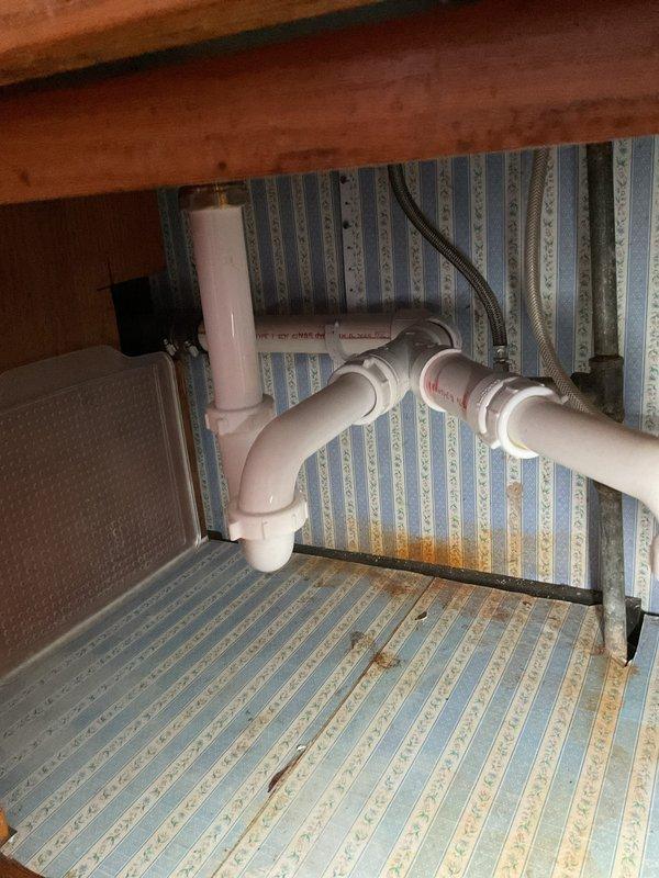 Responded to service call for kitchen sink draining slowly in 60-year-old home. Upon arrival, inspected under-sink plumbing and identified standard P-trap configuration with white PVC pipes and connections. Removed and cleared P-trap assembly of accumulated debris and buildup causing the slow drainage. Inspected drain lines for additional blockages and verified proper water flow. Reassembled all plumbing connections, checked for leaks, and tested sink drainage to confirm issue resolved. All components functioning properly upon completion.