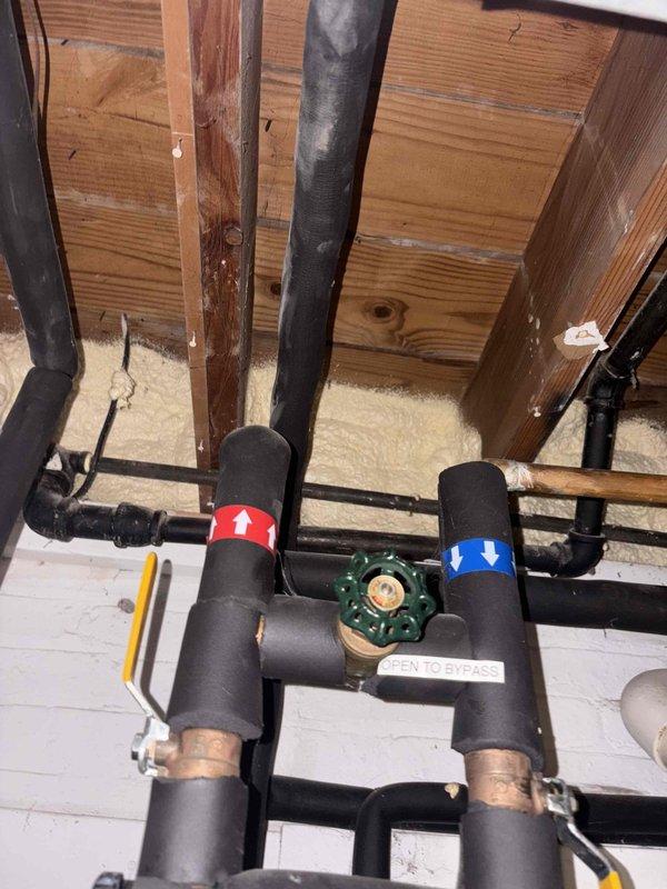 Conducted quality assurance inspection of recently completed water repipe installation, water filtration system, and ice maker line connections. Documented plumbing system featuring new copper piping with foam insulation, backflow prevention valve assembly with bypass capability, and proper hot/cold water line identification in basement crawl space area. Verified under-sink P-trap configuration and supply line connections are functioning correctly per installation specifications.