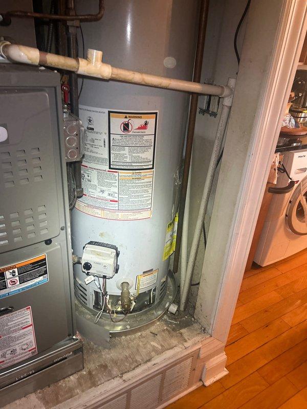 Responded to building-wide hot water outage affecting residential property. Upon arrival, inspected 5-year-old tanked water heater located in first-floor hallway utility closet. Performed diagnostic assessment of unit, examining anode rod condition, gas connections, pilot light assembly, and thermocouple function. Verified proper gas supply and electrical connections to unit. Inspected all visible plumbing connections, including brass fittings, shut-off valves, and supply lines for signs of corrosion or failure. Tested temperature and pressure relief valve operation and examined expansion tank connections. Documented equipment condition with photographs showing water heater installation, surrounding HVAC equipment, and detailed views of lower plumbing connections including blue expansion tank and brass fittings. Restored hot water service to building. Unit operational at time of departure.