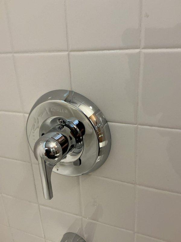 Responded to service call for malfunctioning Kohler single-handle shower valve with improper hot/cold water mixing and reduced hot water flow. Diagnosed cartridge failure causing temperature control issues and restricted flow on hot side. Removed chrome lever handle and circular escutcheon plate from white subway tile wall. Extracted and replaced defective valve cartridge with manufacturer-specified replacement part. Tested temperature mixing across full range of handle positions and verified proper hot water flow and pressure. Reassembled trim components and confirmed leak-free operation.