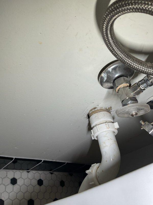 Responded to service call for bathroom plumbing assessment. Inspected traditional two-handle chrome faucet assembly with porcelain handle inserts and evaluated sink basin condition. Examined under-sink plumbing connections including chrome-plated angle stop valve, braided stainless steel flexible supply lines, and PVC drain assembly with elbow joint. Documented existing conditions showing minor mineral deposits at pipe connections, aged caulking at sink-to-wall interface, and normal wear on plumbing components. Photographed faucet fixture and under-sink plumbing configuration for service records.