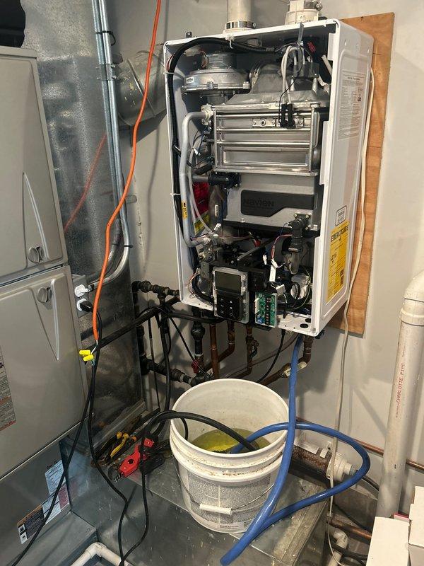 Performed warranty service inspection on tankless water heater unit. Accessed internal components to assess warrantied repair requirements. Identified rust-colored staining and corrosion on appliance surfaces beneath PVC drainage piping system. Documented existing conditions including discoloration on piping and metal hose clamp connections. Advised customer that repair work is required but non-emergency, with scheduling to be arranged by office for completion of warrantied work.