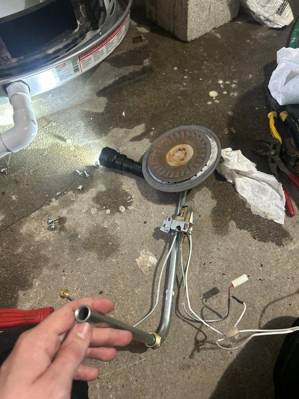 Responded to service call for non-functioning tanked water heater with active leak in basement of 80-year-old residence. Upon inspection, identified failed burner assembly with significant corrosion and deterioration at combustion chamber. Disassembled burner unit and removed defective thermocouple component. Assessed water heater condition in confined utility space with limited access, noting aged infrastructure and compromised burner integrity. Documented equipment failure through photographic evidence showing corroded burner disc and failed safety components. Leak source traced to tank failure related to prolonged operational issues over four-day period.