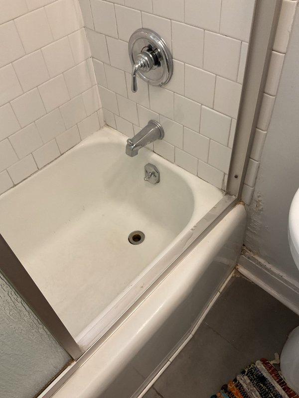 Responded to a slow-draining bathtub in a first-floor bathroom of an approximately 110-year-old residential property. Upon arrival, inspected the chrome tub fixtures and white subway-tiled alcove bathtub installation to assess drainage performance. Accessed the drain system from below through the crawl space or basement area to evaluate the existing plumbing infrastructure. Located the vertical drain stack consisting of white PVC piping with visible securing straps running through the floor joists. Cleared the obstruction causing the slow drainage condition using appropriate drain cleaning methods. Verified proper water flow and drainage function upon completion. The bathtub now drains at normal operating speed with no backup or standing water issues remaining.