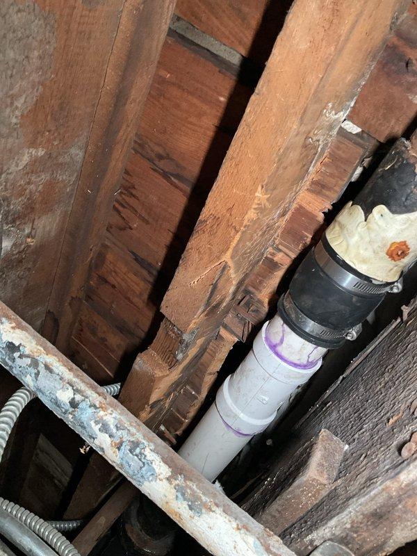 Responded to a slow-draining bathtub in a first-floor bathroom of an approximately 110-year-old residential property. Upon arrival, inspected the chrome tub fixtures and white subway-tiled alcove bathtub installation to assess drainage performance. Accessed the drain system from below through the crawl space or basement area to evaluate the existing plumbing infrastructure. Located the vertical drain stack consisting of white PVC piping with visible securing straps running through the floor joists. Cleared the obstruction causing the slow drainage condition using appropriate drain cleaning methods. Verified proper water flow and drainage function upon completion. The bathtub now drains at normal operating speed with no backup or standing water issues remaining.