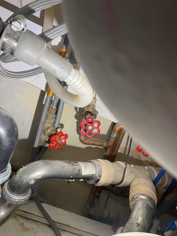 Completed faucet service at residential bathroom with pedestal sink installation. Building water supply was shut down at 11 AM to facilitate the work. Serviced dual shut-off valves with red handles connected to copper supply lines, inspecting braided stainless steel flexible hoses and metal hose clamps for proper connection and function. Verified proper operation of hot and cold water supply lines and drainage system components including white corrugated flexible tubes. All plumbing connections beneath sink were inspected and confirmed secure with no visible leaks upon restoration of water service.