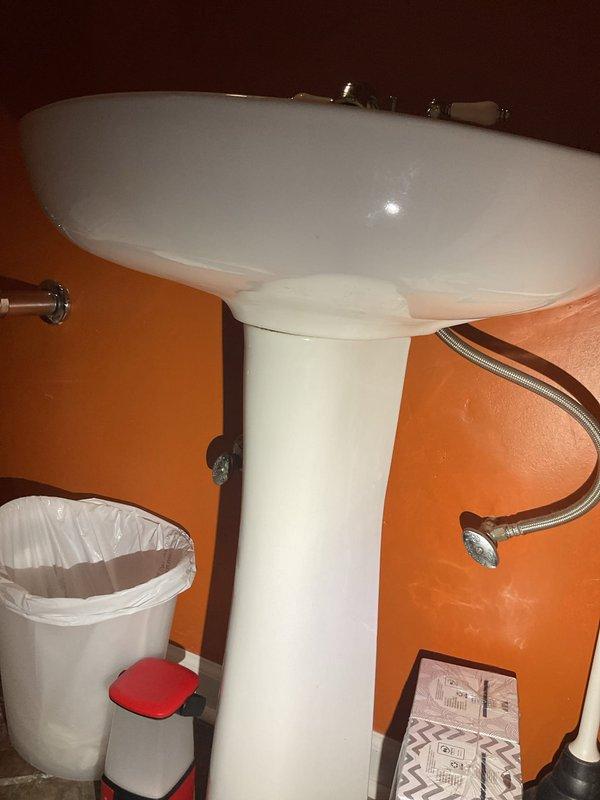 Completed faucet service at residential bathroom with pedestal sink installation. Building water supply was shut down at 11 AM to facilitate the work. Serviced dual shut-off valves with red handles connected to copper supply lines, inspecting braided stainless steel flexible hoses and metal hose clamps for proper connection and function. Verified proper operation of hot and cold water supply lines and drainage system components including white corrugated flexible tubes. All plumbing connections beneath sink were inspected and confirmed secure with no visible leaks upon restoration of water service.