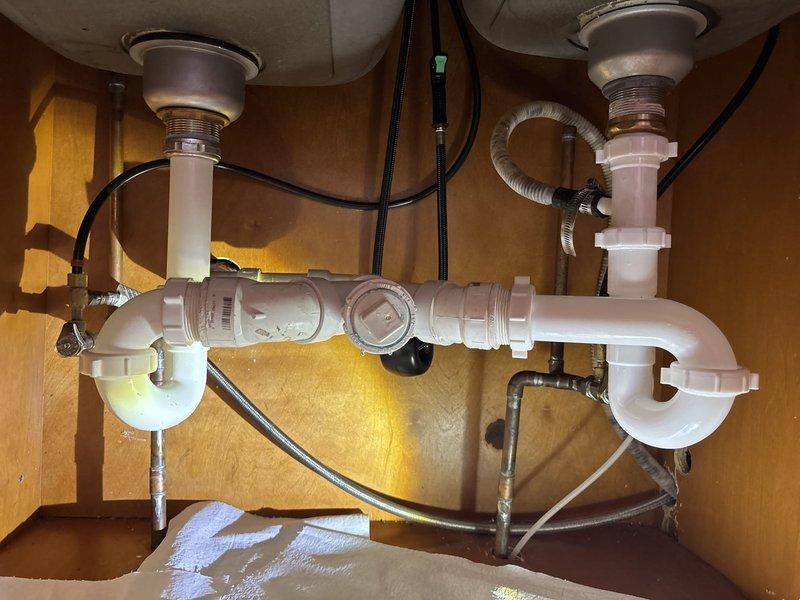 Responded to service call for kitchen sink leaking from underneath. Upon inspection, examined double-basin sink plumbing system and identified leak source at P-trap connection. Disassembled trap assembly, cleared minor debris accumulation, and inspected all PVC drain fittings for proper sealing. Reassembled drain system with secure connections, tested both basins for proper drainage and verified all joints were leak-free under running water.