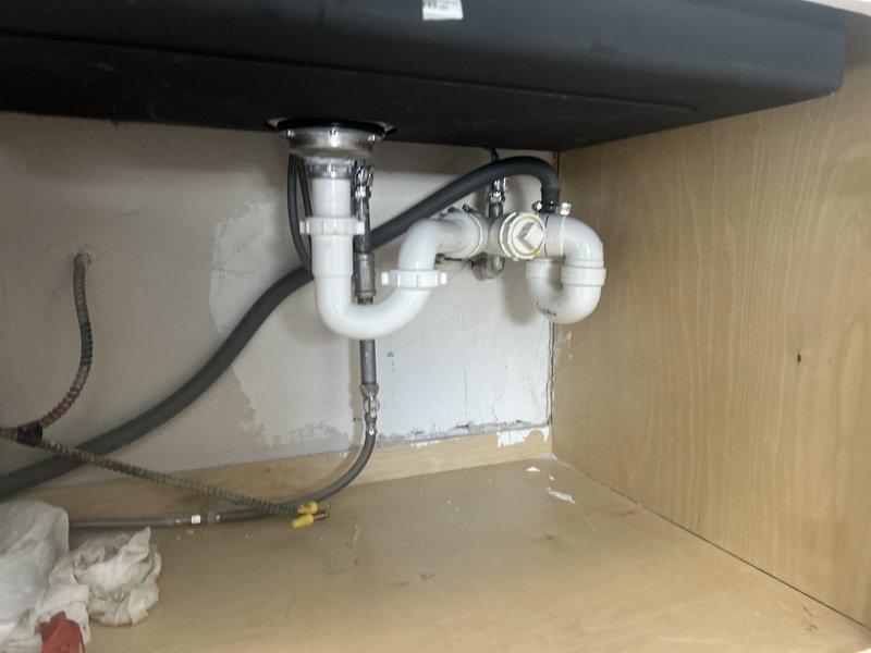 Completed installation of new under-sink plumbing components including white PVC P-trap assembly with chrome fittings and inline bottle trap with valve mechanism. Replaced flexible supply lines and reconnected all drain and water supply connections to ensure proper function and prevent leaks.