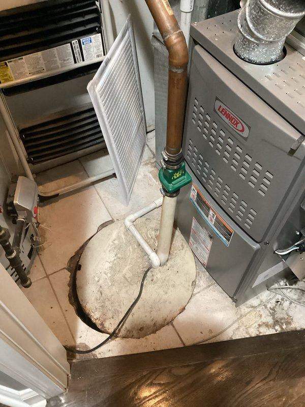 Completed inspection of aging sump pump system with compromised basin cover. Documented existing pump condition showing signs of significant age, corrosion on metal components, and standing water with sediment accumulation in the basin. The pump remains operational despite advanced wear, but the damaged lid presents safety concerns and does not provide proper coverage of the sump pit opening. Photographed mechanical room setup including pump location, adjacent HVAC equipment, and drainage components to provide comprehensive documentation for replacement estimate.