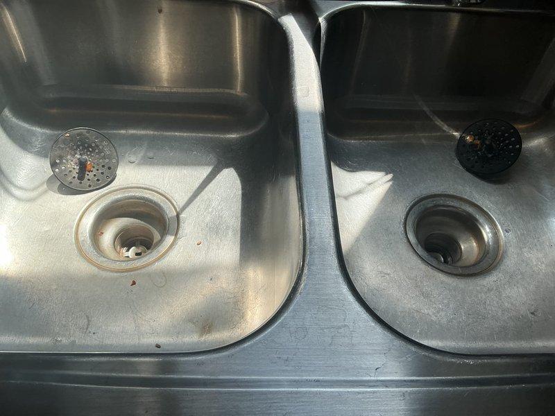 Responded to kitchen sink water leak caused by cracked pipe in the cabinet below. Upon inspection, identified damaged drain line in the P-trap assembly beneath the dual-basin stainless steel sink. Assessed both left and right side plumbing configurations, noting the chrome and plastic drain components and existing trap assemblies. Documented existing conditions including mineral deposits and surface oxidation on metal fittings. Replaced the compromised pipe section to eliminate the active leak and restore proper drainage function. Tested system for proper water flow and verified no additional leaks present upon completion.