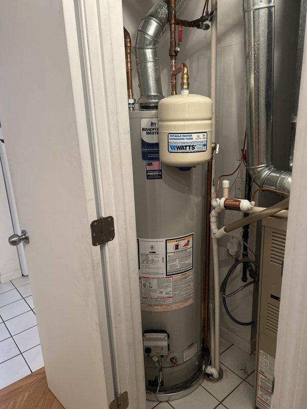 Performed routine maintenance flush on residential tanked water heater to remove sediment buildup and ensure optimal performance. Drained tank completely through bottom drain valve, flushed system with fresh water until discharge ran clear, and verified all copper supply lines, brass fittings, and connections for leaks. Inspected WATTS expansion tank, confirmed proper pressure relief valve operation, and documented equipment condition with pre- and post-service photographs showing installation in utility closet alongside HVAC system.