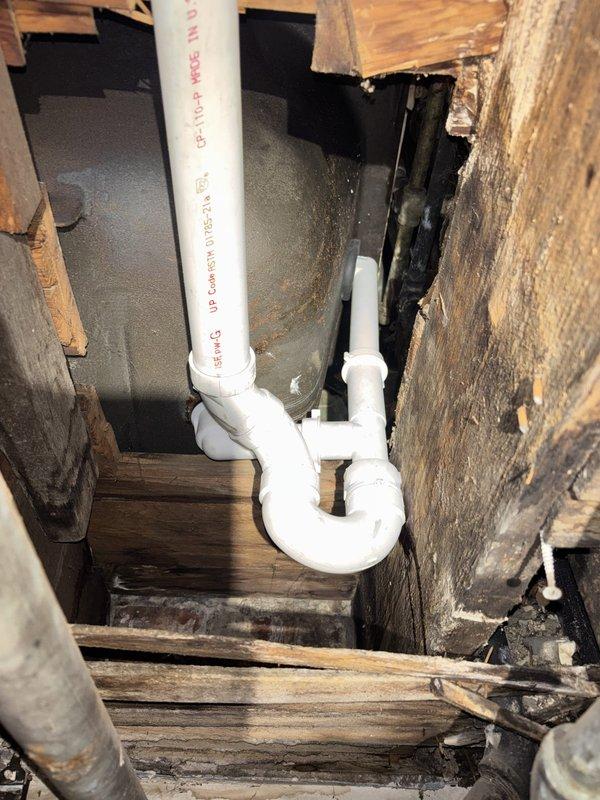 Responded to callback for drum trap removal and waste overflow replacement. Removed obsolete drum trap assembly from basement plumbing system and installed new PVC P-trap configuration with proper waste and overflow connections. New installation features white PVC piping with appropriate fittings and red coupling valve for system control. Work completed in utility room area with all connections properly sealed and tested for leaks.