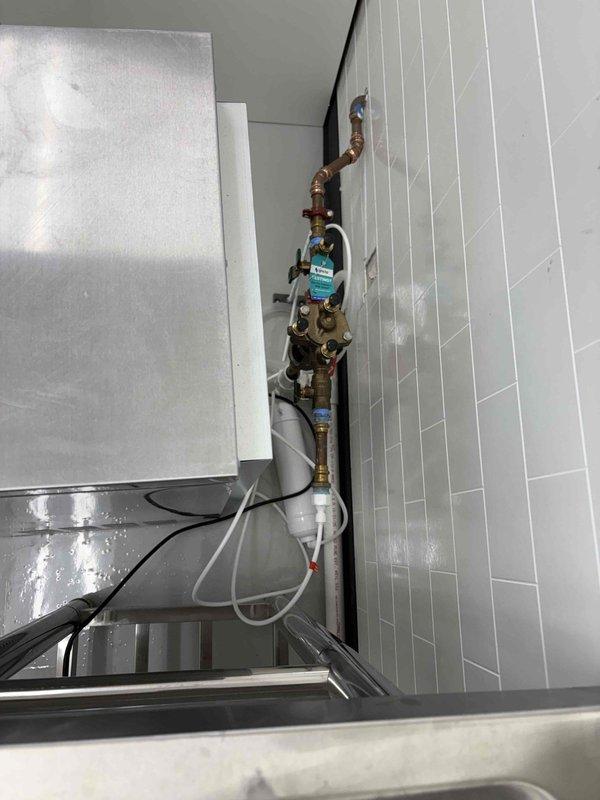 Licensed plumber completed final inspection of plumbing installation in mechanical room and commercial kitchen area. Verified proper installation of water heater system with copper piping, pressure relief valve, brass ball valves, and associated fittings mounted to specification. Inspected commercial-grade stainless steel sink unit with pull-down faucet, confirmed water supply lines, drainage connections, and all plumbing components meet code requirements for final approval.