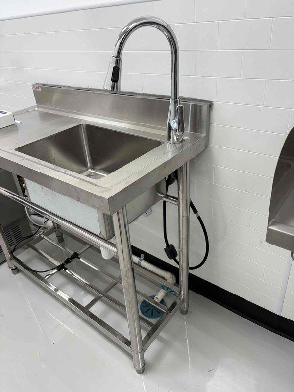 Licensed plumber completed final inspection of plumbing installation in mechanical room and commercial kitchen area. Verified proper installation of water heater system with copper piping, pressure relief valve, brass ball valves, and associated fittings mounted to specification. Inspected commercial-grade stainless steel sink unit with pull-down faucet, confirmed water supply lines, drainage connections, and all plumbing components meet code requirements for final approval.