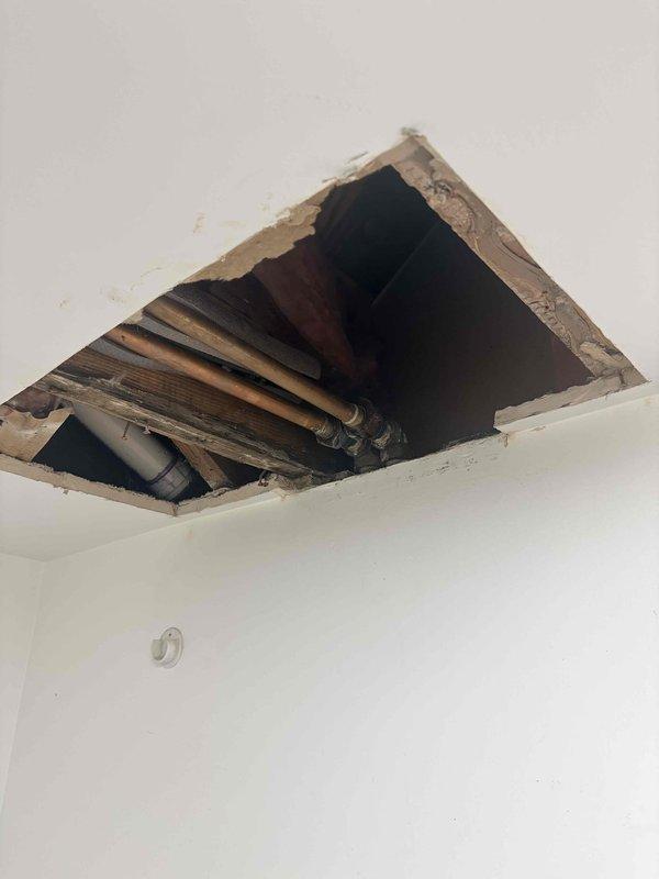 Conducted site assessment of laundry room plumbing system following initial service request. Documented existing conditions including exposed ceiling cavity above utility space, revealing copper supply piping and structural framing members. Photographed accessible plumbing infrastructure through ceiling access point and overall room configuration to support estimate preparation for proposed piping modifications or repairs.