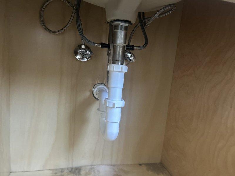 Completed faucet installation at exterior hose bib location and kitchen sink. Installed new brass hose connector and valve assembly at outdoor spigot mounted to brick exterior wall, ensuring proper weatherproofing and secure connections. Under kitchen sink, installed new faucet with chrome supply lines, braided stainless steel flexible hoses, shut-off valves, and integrated the cylindrical mounting assembly with existing PVC drain system and P-trap configuration.
