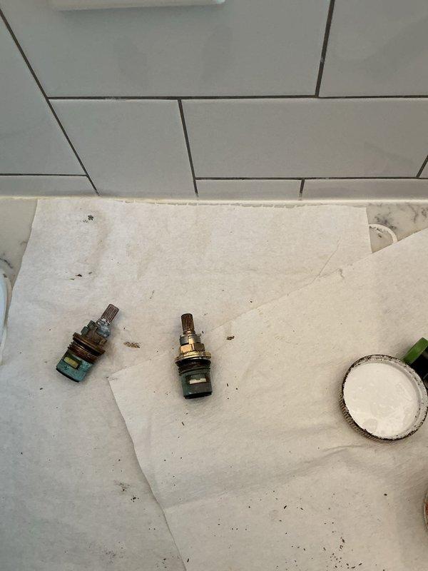 Responded to service call regarding black water discharging from bathroom faucet. Upon inspection, diagnosed issue as failed faucet cartridges causing sediment and mineral buildup to contaminate water flow. Removed and replaced two deteriorated brass cartridges from wall-mounted three-piece faucet assembly installed on white subway tile backsplash. Old cartridges exhibited significant corrosion and greenish-blue oxidation on lower sections, indicating extended service life and internal component breakdown. Installed new cartridges, tested all handle controls and spout operation for proper function and water clarity. Verified no leaks at mounting points and confirmed water now runs clear without discoloration. Determined filtration system not necessary as issue was isolated to localized cartridge failure rather than main water supply contamination.