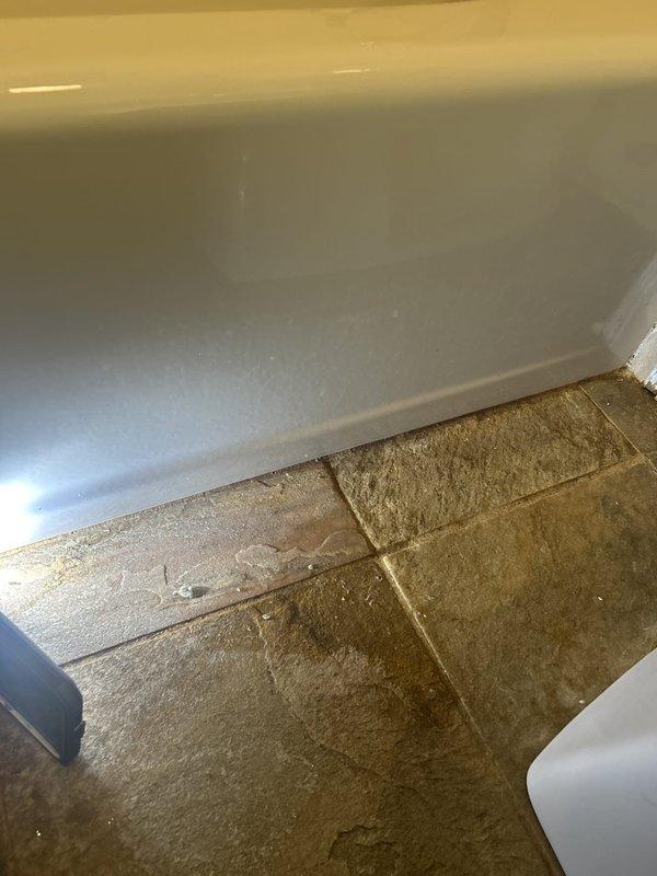 Responded to water leak complaint at bathtub area where water was observed coming from the side of the tub during shower use. Performed visual inspection of the tub-to-wall junction and surrounding areas. Documented existing conditions including the tub surround interface with tile flooring, caulking along baseboards, and ceiling damage above the bathroom showing diagonal cracking and water staining indicative of active or previous moisture intrusion. Identified potential failure points at tub enclosure seals that could allow water migration during shower operation. Photographed evidence of leak pathways and resulting structural damage for repair recommendations.