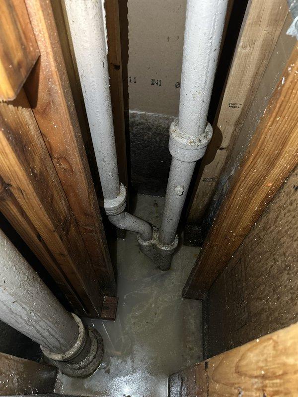 Responded to water intrusion issue in basement with visible pooling near baseboard and audible trickling behind walls. Performed comprehensive leak location inspection of plumbing system in crawlspace and basement area. Visual examination revealed moisture damage and dark staining on floor joists, PVC piping, and wooden structural components near pipe penetrations. Inspected multiple pipe junctions and fittings for signs of active leakage. Documented water damage patterns and deterioration on building infrastructure components. Identified areas of concern requiring further evaluation to determine if source is supply line failure or groundwater seepage through foundation.