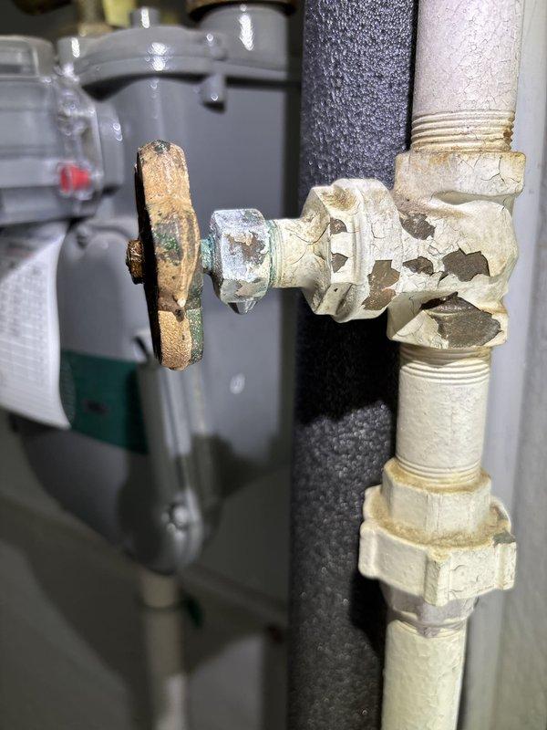 Responded to basement water leak complaint and identified source as heavily corroded valve assembly with active leakage at threaded bolt connection. Upon inspection, found extensive corrosion on valve body and brass handle with rust staining and mineral deposits throughout the plumbing system, indicating aged infrastructure. Documented existing conditions including deteriorated valve assembly, corroded piping connections, and compromised seals at threaded fittings for repair recommendation.