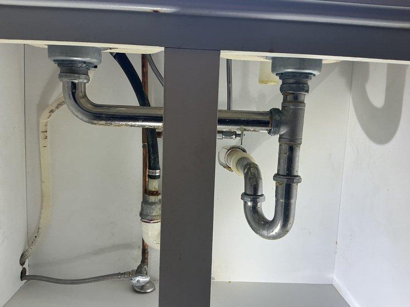 Completed under-sink plumbing repair involving P-trap assembly replacement and drain line service beneath dual bathroom sink. Utilized professional plumbing tools to remove and reinstall chrome-finished P-trap configuration, addressing drainage issues and ensuring proper trap seal for both sink basins.