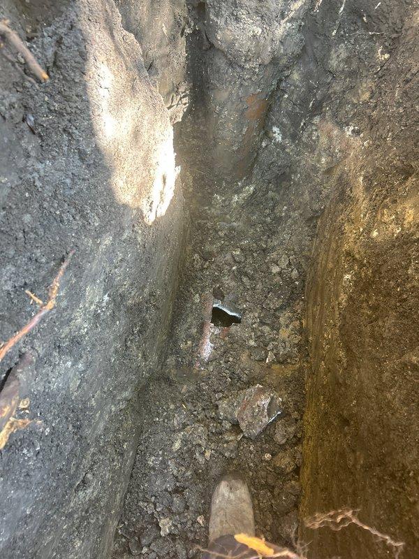 Excavated trench to access underground plumbing infrastructure for repair or replacement of damaged pipe fitting. Addressed exterior vent pipe deterioration and foundation penetration issues, including weathered pipe cap and algae growth on adjacent siding that indicated potential moisture concerns requiring attention.