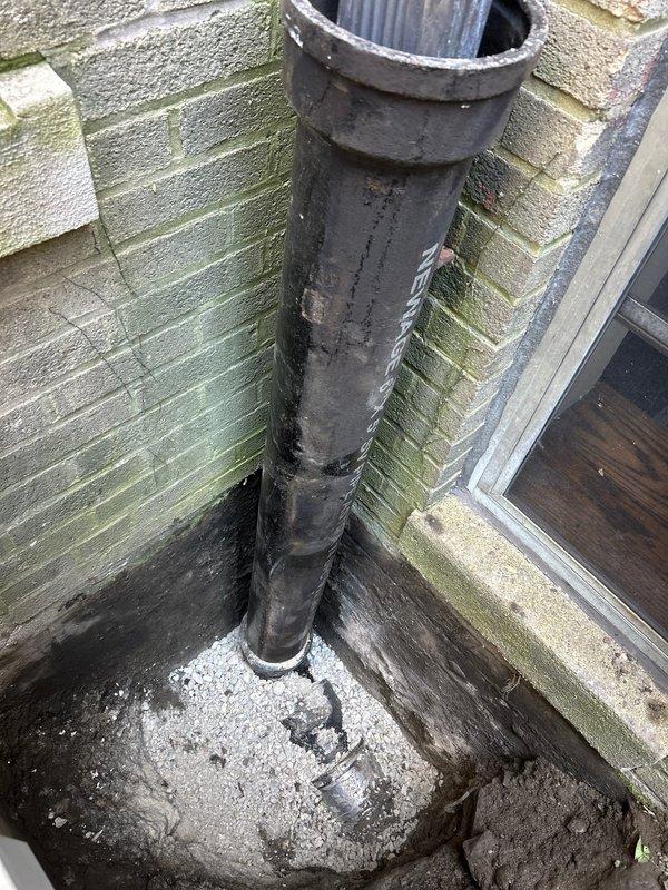 Excavated trench to access underground plumbing infrastructure for repair or replacement of damaged pipe fitting. Addressed exterior vent pipe deterioration and foundation penetration issues, including weathered pipe cap and algae growth on adjacent siding that indicated potential moisture concerns requiring attention.
