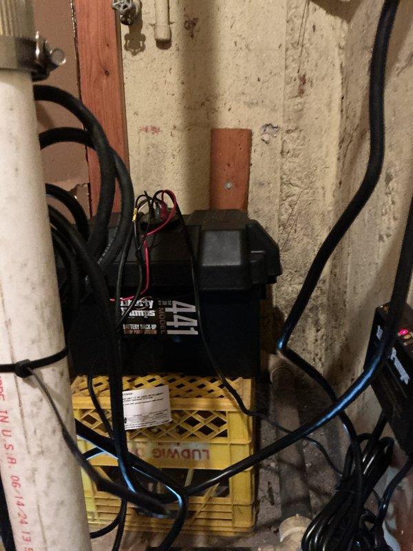 Responded to service call for non-functional sump pump battery backup system. Upon inspection, identified failed backup control unit and deteriorated electrical connections affecting the emergency power supply. Evaluated the primary sump pump assembly housed in cylindrical basin with associated discharge piping and verified main pump operational status. Assessed battery backup controller mounted on utility crate, noting compromised wiring connections and potential power supply failure to backup pump motor. Documented existing system configuration including PVC discharge lines, electrical routing, and backup component placement for estimate preparation. Provided customer with detailed assessment of battery backup system failure and recommended replacement of backup control unit and associated electrical components to restore emergency pumping capability during power outages.