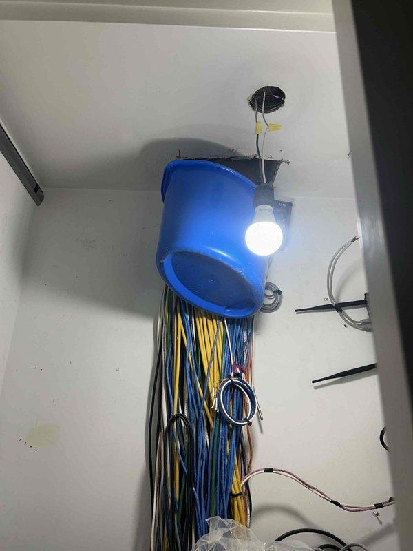 Responded to a boiler system pipe leak in a utility room. Upon inspection, identified active water leak from overhead piping and implemented temporary containment using a suspended collection bucket to prevent water damage to electrical components and surrounding areas. Documented the installation setup showing multiple electrical conduits and wiring systems in close proximity to the leak source, emphasizing the need for immediate leak resolution to protect the electrical infrastructure.