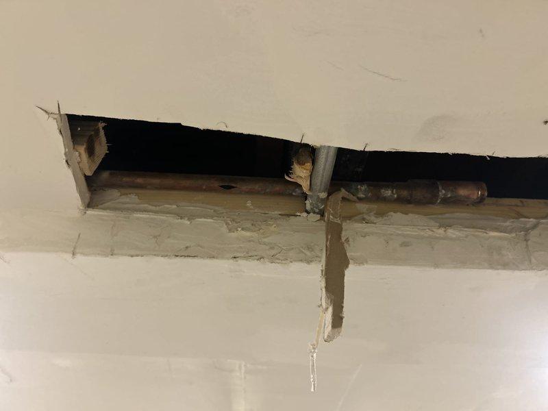 Accessed corroded horizontal supply line through wall opening to assess pipe condition and identify source of plumbing issue. Documented severely deteriorated metal piping with extensive corrosion, rust buildup, and mineral deposits requiring replacement. Cut access openings in ceiling and wall to expose affected plumbing infrastructure, revealing compromised copper supply lines and associated piping that necessitate full repair and restoration of water distribution system in affected area.