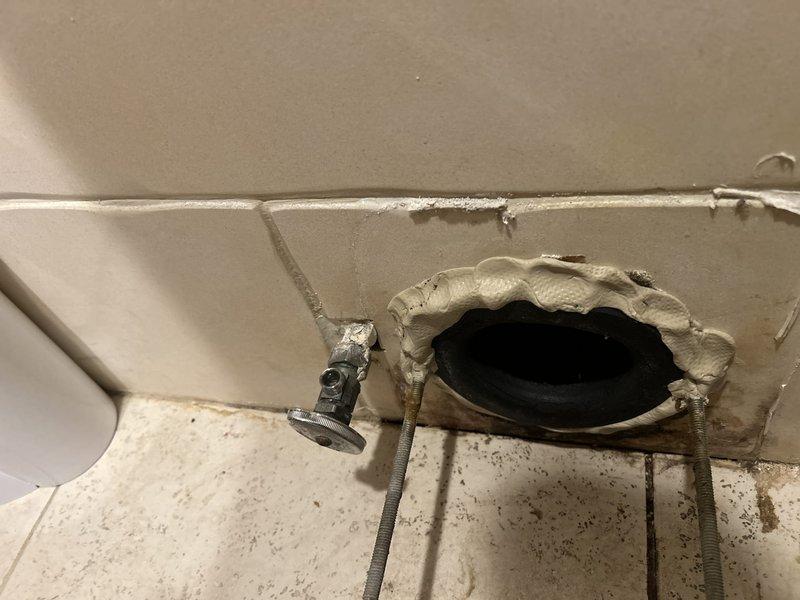 Diagnosed toilet supply line issue requiring replacement parts. Accessed plumbing connection through wall opening to evaluate water supply valve and surrounding area showing signs of water damage and mineral deposits. Parts have been ordered and follow-up appointment scheduled to complete installation of new supply line components and restore wall surface.