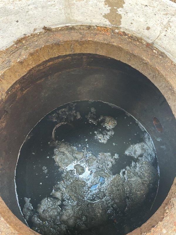 Completed comprehensive ejector pump inspection, accessing the below-grade pump basin through the existing concrete access pit. Visual assessment revealed standing water in the sump basin with visible debris accumulation and sediment present in the collection chamber. Documented current system conditions including deteriorated concrete collar edges, moisture levels, and water quality within the ejector pit, noting rust staining around the access opening perimeter. Photographic documentation captured for service records showing basin interior conditions and water accumulation levels.