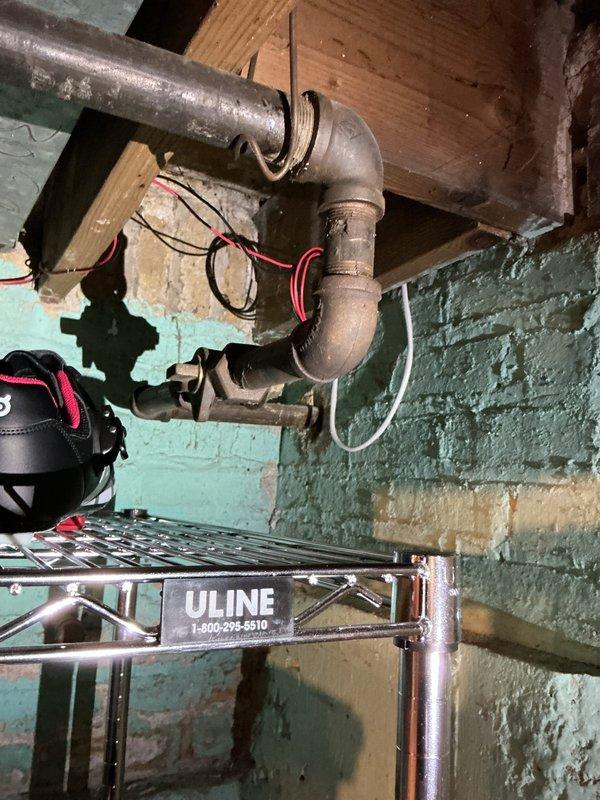 Performed pressure test on gas line system to verify integrity and identify potential leaks. Inspected interior gas piping configuration in basement utility area, including aged copper/brass connections and P-trap assembly with multiple fittings. Conducted exterior inspection of gas meter installation, pressure regulator, and associated white PVC piping mounted on building exterior. Documented existing conditions of gas distribution system through photographic evidence showing both interior piping connections and exterior meter assembly to establish baseline for pressure testing procedures.