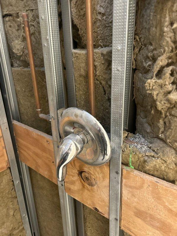Completed plumbing rough-in installation for shower valve assembly in basement renovation area. Installed chrome mixing valve with trim on framed wall structure, ran copper supply lines vertically through metal stud framing, and coordinated with insulation contractor for spray foam application around plumbing penetrations to ensure proper thermal envelope while maintaining access to water lines.