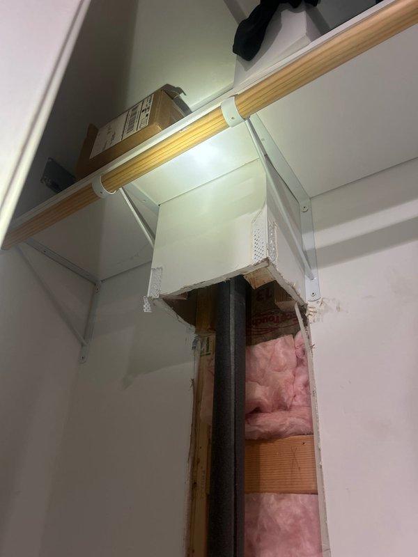 Completed repair of damaged b-box cap assembly with access through interior wall cavity. Removed drywall section to expose plumbing chase containing vertical yellow gas line with chain-style valve and horizontal galvanized water supply pipe. Repaired and secured b-box cap, verified proper operation of shutoff mechanism, and confirmed no leaks present. Wall cavity left accessible for inspection, with pink fiberglass insulation and structural components visible for future maintenance access.