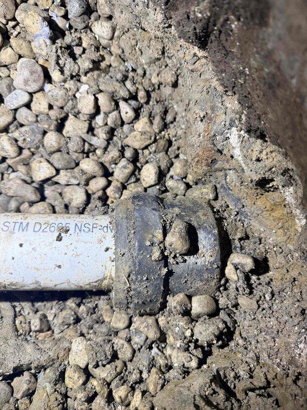 # Drain and Sewer Estimate Residential

Conducted site assessment of underground sewer system following identification of improper existing pipe installation. Investigation revealed defective sewer pipe beneath concrete flooring requiring excavation for proper access and evaluation. Documented deteriorated conditions including exposed PVC piping, compromised floor surfaces with aggregate substrate visible, and white PVC pipe fittings marked STM D2665 NSF-61 lying on gravel bedding. Assessment confirmed concrete removal will be necessary to fully expose the drain line for repair or replacement. Photographic documentation captured the extent of floor deterioration, exposed plumbing infrastructure, and compromised pipe components to support scope of corrective work required.