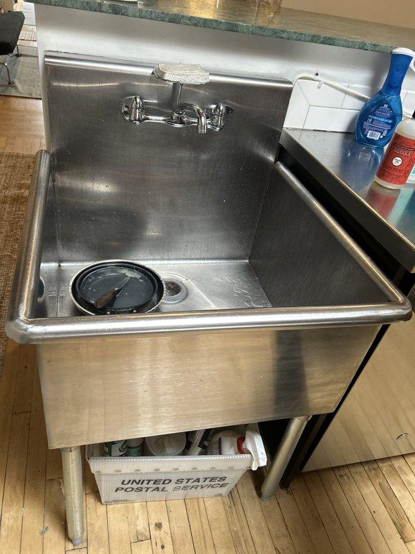Responded to no-water issue at shower/tub location. Upon arrival, discovered the problem was actually related to a commercial stainless steel utility sink with wall-mounted chrome faucet rather than a shower/tub fixture. Inspected the deep basin sink, faucet assembly with dual cross-handle controls, and drainage system. Documented existing conditions including water stains, mineral deposits, and general wear patterns on stainless steel surfaces. Verified drain strainer and basin functionality, examined wall-mounted faucet installation and water supply connections to diagnose the reported water flow issue.