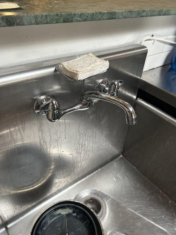 Responded to no-water issue at shower/tub location. Upon arrival, discovered the problem was actually related to a commercial stainless steel utility sink with wall-mounted chrome faucet rather than a shower/tub fixture. Inspected the deep basin sink, faucet assembly with dual cross-handle controls, and drainage system. Documented existing conditions including water stains, mineral deposits, and general wear patterns on stainless steel surfaces. Verified drain strainer and basin functionality, examined wall-mounted faucet installation and water supply connections to diagnose the reported water flow issue.