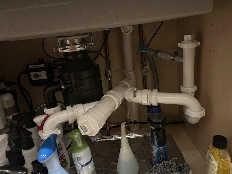 Responded to kitchen sink leak reported two days prior in residential property. Upon inspection, identified failed connection at braided supply line fitting beneath sink. Removed defective supply line connector and replaced with new chrome-plated flexible connector assembly featuring reinforced braided hose construction. Verified all connections to drain assembly, P-trap, and garbage disposal unit for additional leak sources. Tested water supply system under pressure to confirm proper seal at all connection points. Cleared cabinet area of cleaning supplies during repair work and returned items to storage position upon completion. System restored to full operation with no active leaks detected.