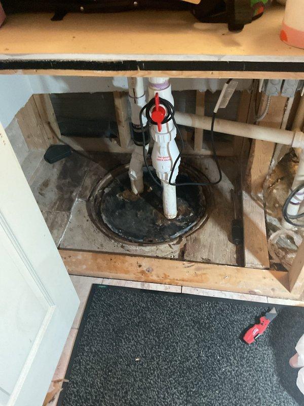 Responded to service call for gurgling drains and non-operational pump in basement utility area. Upon inspection, identified issues with sump pump system and associated PVC drainage piping. Documented existing plumbing configuration including vertical waste lines with attached electrical wiring and pump installation with red valve mechanism. Assessed pump functionality and drainage system performance. Photographed installation showing pump basin, discharge piping, and check valve assembly for diagnostic and documentation purposes.