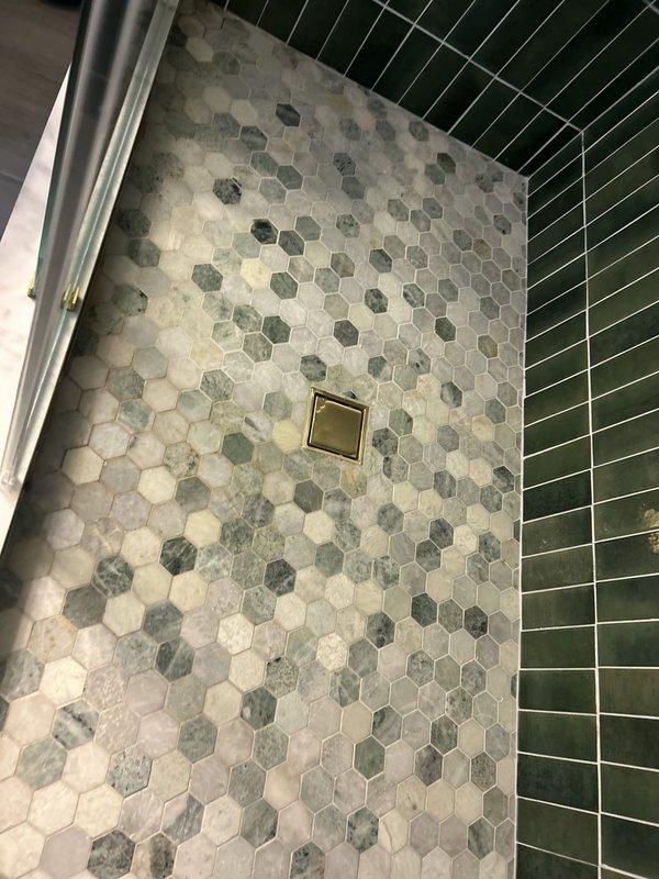 Responded to active water leak in utility room of 50+ year old residence. Upon arrival, observed significant water staining and discoloration on concrete floor surrounding furnace and hot water heater equipment. Conducted thorough visual inspection of all visible plumbing components including white PVC drain lines, copper supply tubing, and brass fittings connected to water heating equipment. Traced water damage patterns across utility room floor to identify potential leak source. Inspected all accessible piping connections, joints, and equipment interfaces for signs of active moisture or dripping. Also inspected bathroom plumbing fixtures including shower area with hexagonal tile flooring and drain assembly to rule out secondary leak sources. Documented findings with photographs showing extent of water damage and condition of plumbing systems. Leak location service completed with findings reported to property owner for next steps regarding repair recommendations.