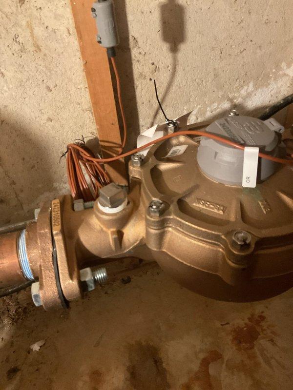 Responded to water leak in crawl space affecting previously installed piping system. Upon inspection, identified active leaks at two locations: a brass shut-off valve assembly and a threaded joint connection on copper piping near a sewage ejector pump. The valve showed visible moisture accumulation and floor staining beneath the installation point. The joint connection exhibited corrosion and patina on copper surfaces, with evidence of water intrusion around metal fittings and clamps. Documented conditions with photographs showing the valve assembly mounted against concrete wall with connected copper tubing and the orange ejector pump system with compromised pipe connections. Assessment completed and repair recommendations provided for both leak points to restore system integrity.