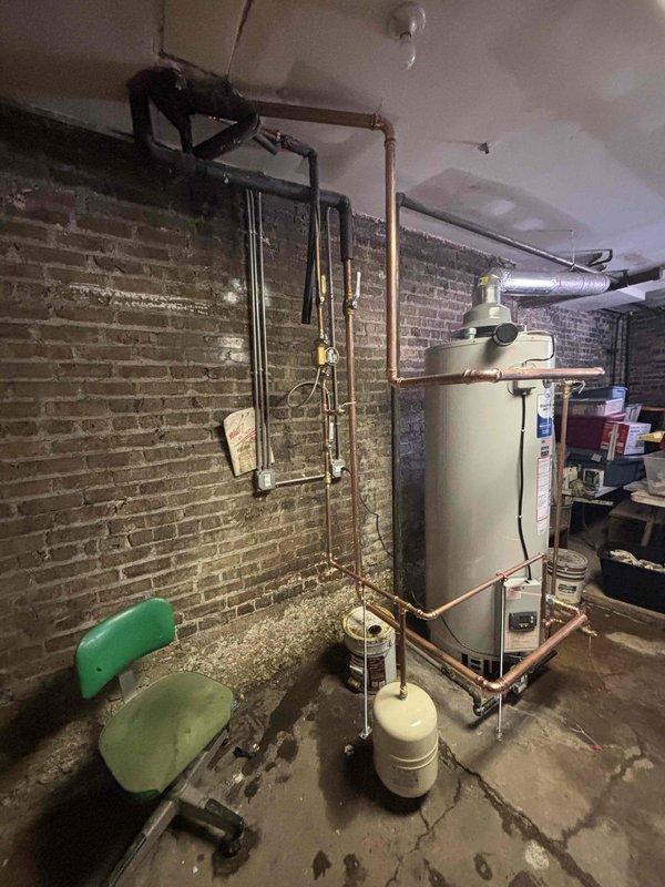Installed a 100-gallon tanked water heater in basement utility room with complete copper piping connections and white expansion tank positioned at base of unit. All supply and discharge lines were properly configured with appropriate valves and fittings, and system was tested for proper operation and leak-free connections upon completion.